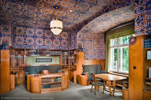 Arbeitszimmer von Karl Ernst Osthaus im Hohenhof - Am Stirnband, Hagen - Das Arbeitszimmer ist Höhepunkt der Raumabfolge im Erdgeschoss. Die eingebauten Möbel aus grau polierter Esche hatten einen grünlichen Grundton. Gegen den Protest des Architekten van de Velde, der für die Raumdecke ein gebrochenes Weiß vorsah, ließ Osthaus 1911 eine in orange, graugrün und blau gehaltene Schablonenmalerei von Johan Thorn Prikker auftragen. Foto © Dietrich Hackenberg