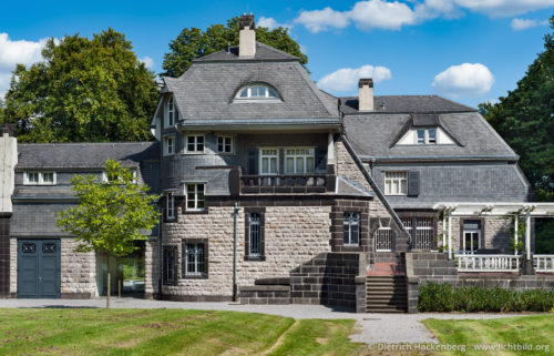Hohenhof - Aussenansicht Westflügel - Das Gebäude besteht aus dem Kalkstein, gestaltet als massives Bruchsteinmauerwerk. Die harmonische Verbindung des Baumaterials mit glatter, schwarzer Niedermendiger Basaltlava und dem bläulichen Moselschiefer des Daches sowie den Farben weiß und moosgrün für Türen und Fenster steht in der bergisch-märkischen Tradition. Zentrales Bauwerk des Hagener-Impulses. Foto © Dietrich Hackenberg