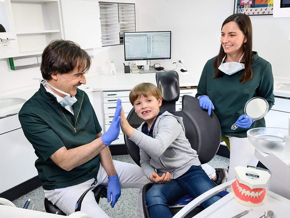 Kinderzahnheilkunde - Zahnarzt abklatschen mit jungem Patienten