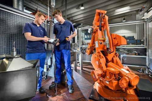 Der Meister erklärt dem Auszubildenden anhand der Fernbedienung den Roboter — „Kurs auf Ausbildung“, Rasspe Systemtechnik GmbH - Group Schumacher