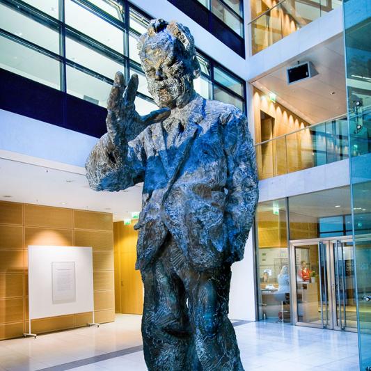 Willy-Brandt-Skulptur von Rainer Fetting - Willy-Brandt-Haus, Wilhelmstr. 141, 10963 Berlin - Foto © Dietrich Hackenberg - Von Februar bis Juni 1937 hält sich der aus Deutschland nach Norwegen emigrierte Willy Brandt in Spanien auf. Er sendet regelmäßig Berichte über an seine politischen Freunde in Paris, dem Sitz der SAP (Sozialistische Arbeiterpartei) Auslandsleitung, sowie an skandinavische Arbeiter und Gewerkschaftszeitungen. Das norwegische Spanien Komitee informiert er über wirksame Hilfsmöglichkeiten für die Bevölkerung. […] Die Lage in Katalonien war verwirrend. Dass es kaum etwas zu Essen gab und der Hunger mit Rotwein, bestenfalls Oliven betäubt werden musste, das es unwürdig war Trinkgeld zu geben und Bedienung durch Händeklatschen herbeizurufen, und allerorts ein ‚Sozialismus der unmittelbaren Produzenten’ angepriesen wurde, nun ja daran gewöhnte man sich rasch. Aber sonst? Es brauchte einige Zeit bis ich zu verstehen begann. […] Willy Brandt über seinen Aufenthalt im Spanischen Bü rgerkrieg In: Links und frei. Mein Weg 1930–1950. Hamburg 1982 […]Lehrreiche, doch überwiegend unglückliche Monate.[…] So fasst Willy Brandt seine Erfahrungen zusammen. In seinen Lebenserinnerungen ergänzt er: […] Nach den Monaten in Berlin und in Barcelona fühlte ich mich meiner Sache sicher und war nicht länger ein Suchender. […]