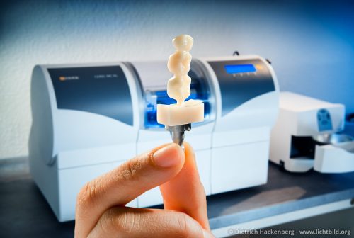 Das fertig gefräste Produkt. Hintergrund die CEREC-Fräse.
